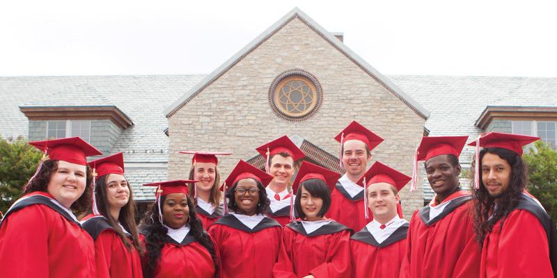 Bryn Athyn College graduates in cap and gown standing in front of Brickman Center