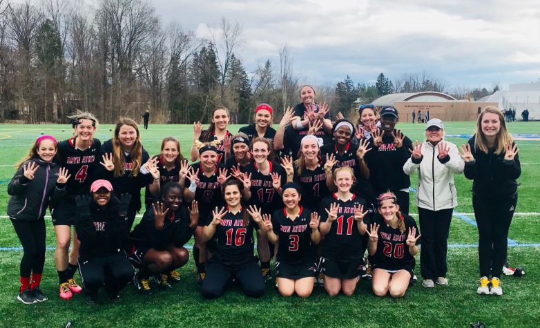 women's lacrosse team posing together with big smiles and holding up eight fingers, signifying their winning streak