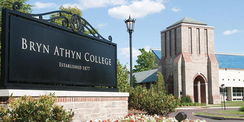 The Bryn Athyn College sign stands in the foreground with the Brickman Center and Swedenborg Library behind it at Bryn Athyn College