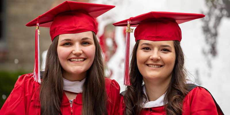 Students at graduation smile in front of the fountain