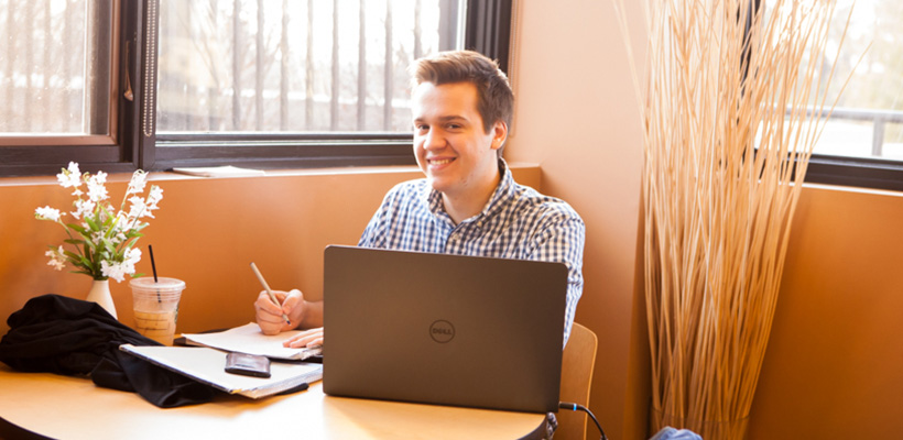 Bryn Athyn College student in the cafe working on a laptop while enjoying an iced tea