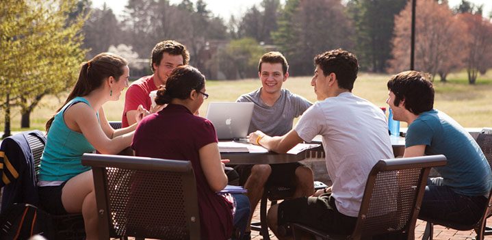 Students working on a group project at a patio table outdoors
