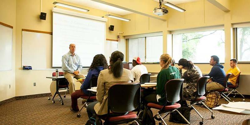 A professor addressing his class in a sunny classroom