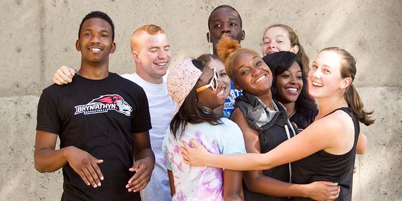 Bryn Athyn College students huddled together and smiling at the camera on a warm day