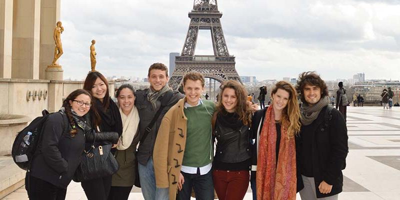 A student studying abroad in France, posing with friends in front of the Eiffel Tower
